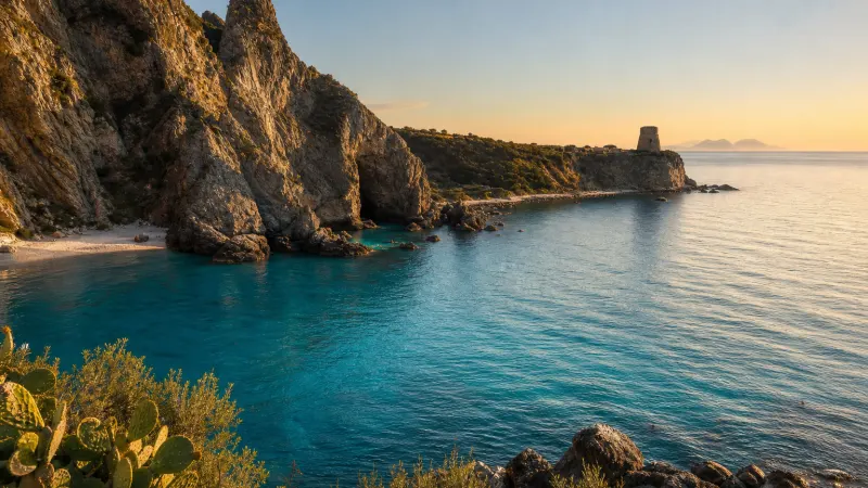 Una delle calette di Briatico al tramonto, con scogli bassi, acqua turchese e un'antica torre di vedetta sul litorale